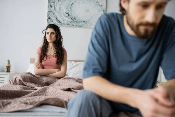 Angry Brunette Woman Crossing Arms While Sitting Blurred Boyfriend Bedroom — Stock Photo, Image