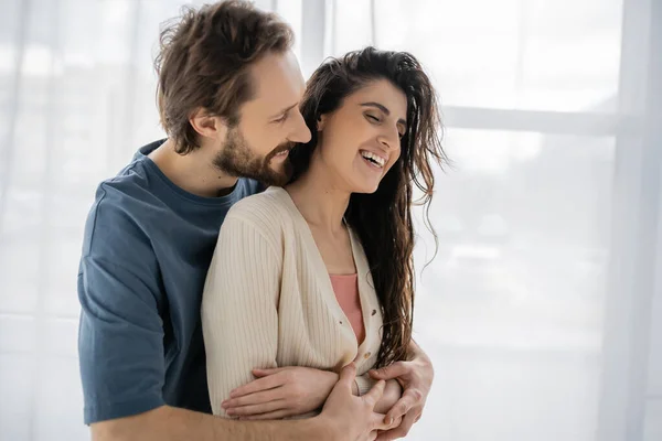 Bearded Man Embracing Overjoyed Brunette Girlfriend Home — Stock Photo, Image