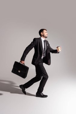 Gülümseyen işadamının yan görünüşü. Gri arka planda çalışan içecek ve evrak çantası.