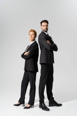 full length of incredulous business people standing back to back with folded arms on grey background clipart