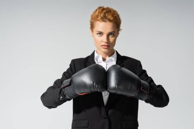 Gri renkli kameraya bakan resmi giyimli ve boks eldivenli ciddi bir iş kadını.