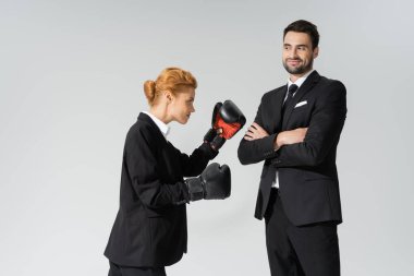 redhead woman in formal wear boxing near cheerful businessman standing with crossed arms isolated on grey clipart