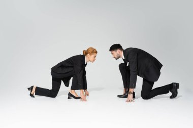 side view of business people in suits standing in low start position and looking at each other on grey background clipart