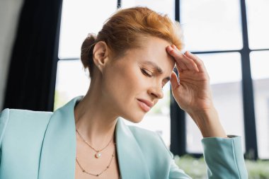 frowning businesswoman with closed eyes touching forehead while suffering from migraine in office clipart