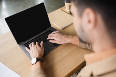 blurred businesswoman typing on laptop with blank screen near notebook on work desk in office clipart