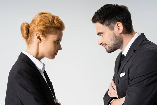 side view of distrustful business people looking at each other isolated on grey