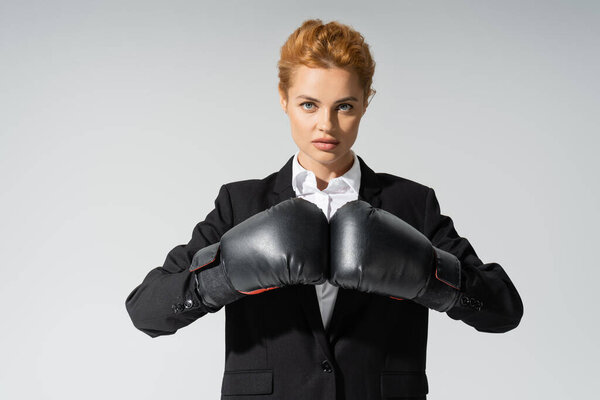 серьезная деловая женщина в формальной одежде и боксерских перчатках глядя на камеру, изолированную на сером