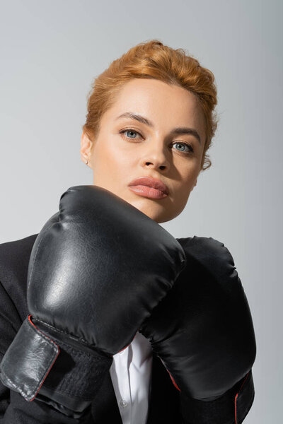 портрет уверенной рыжей предпринимательницы в боксёрских перчатках, смотрящей в камеру, изолированную на сером