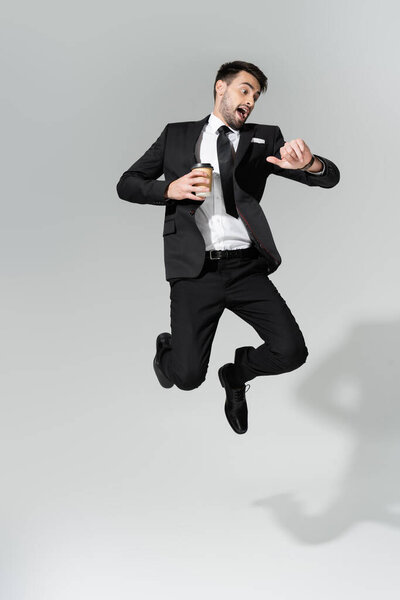 взволнованный бизнесмен с кофе пойти проверить время и левитации на сером фоне