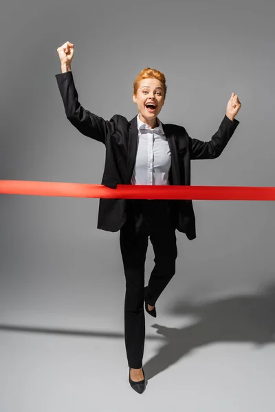 Full Length Cheerful Businesswoman Rejoicing Crossing Finish Ribbon Grey Background — Stock Photo, Image