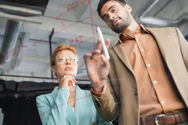 stock image low angle view of businessman with felt pen pointing at lettering on glass board near thoughtful colleague in office