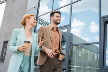 Pozitif kızıl saçlı iş kadını, gülümseyen meslektaşıyla yürürken parmağıyla işaret ediyor.