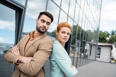 skeptical business people standing back to back with folded arms near building on city street clipart