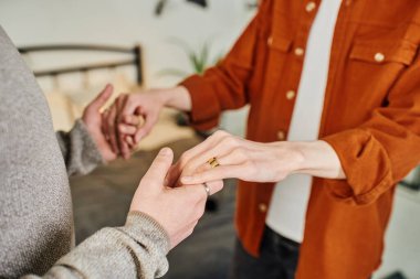 Yatak odasında, evlilik yüzüğünde erkek arkadaşının elini tutan eşcinsel adamın kısmi görüntüsü