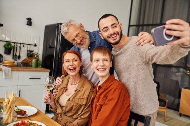 Neşeli eşcinsel adam evde aile yemeği yerken erkek arkadaşıyla selfie çekiyor.