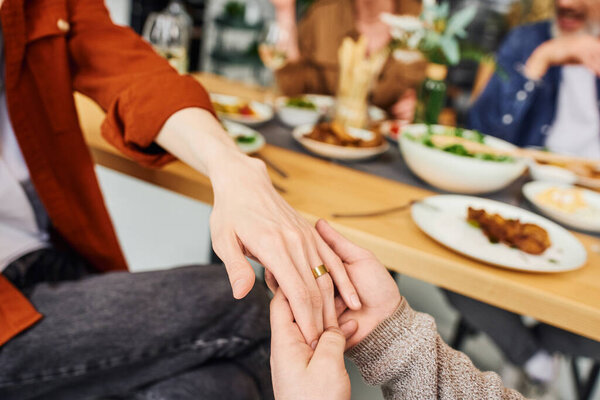 cropped view of gay man holding hand on boyfriend in wedding ring near blurred supper and parents at home