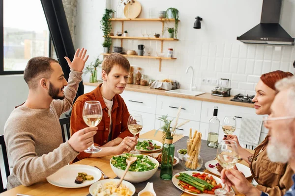 在现代厨房里享用美味的晚餐时 快乐快乐的男人在男朋友和父母身边做手势和祝酒 — 图库照片