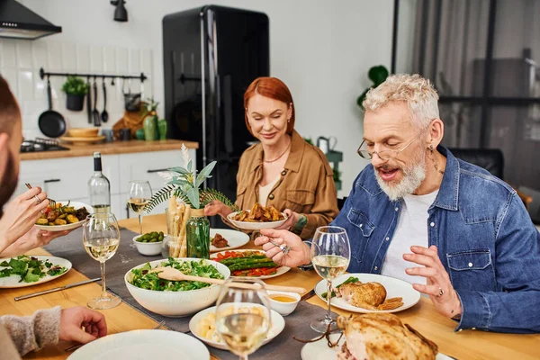 キッチンでおいしい食事をしながら家族と話す眼鏡の陽気な髭の男 — ストック写真