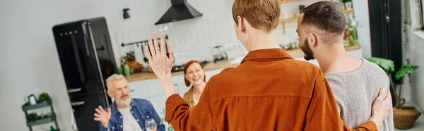 年轻人在厨房里拥抱同性恋伴侣 向快乐的父母挥手 高举横幅 — 图库照片