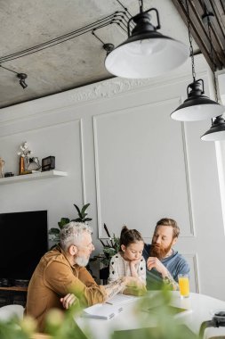 Evde küçük kızıyla ödev yapan aynı cinsiyetten ebeveynler. 