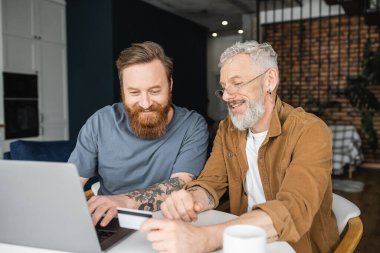 Evde kredi kartı ve laptop kullanan aynı cinsiyetten bir çift. 