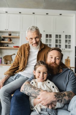 Homoseksüel bir adam gülümseyen kızını kucaklıyor ve evde kameraya bakıyor. 