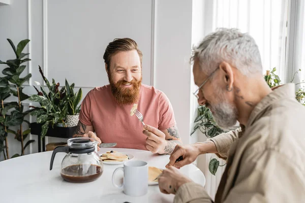 有纹身的同性恋男人在家里吃早餐时看着伴侣 — 图库照片