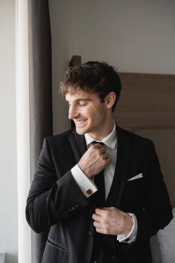 Modern otel odasında gülümserken beyaz gömlekli şık ve yakışıklı bir adam. Düğün gününde damat, özel bir durum.  