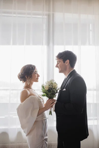 宝石の花嫁のサイドビュー 一緒に立って ホテルで結婚式の後 お互いを見て古典的な正式な摩耗でブライダル花束と新郎と白いドレス 幸せなカップル — ストック写真