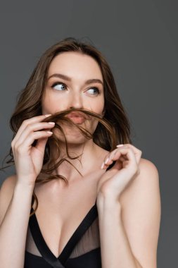 Genç ve seksi esmer kadın portresi günlük makyaj ve modern saç stili ile, dudaklarını bükerek ve saçlarını tutarak gri renkten soyutlanmış bir şekilde yüzünü çeviriyor.  