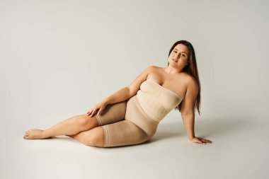 barefoot and confident woman in strapless top with bare shoulders and underwear posing while sitting in studio on grey background, body positive, self-love, plus size  clipart