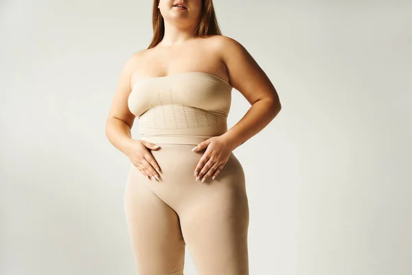 在演播室里 有着超大身材的女人在没有肩带的无袖上衣和灰色背景的内裤中摆姿势 身体呈阳性 双手放在肚子上 — 图库照片