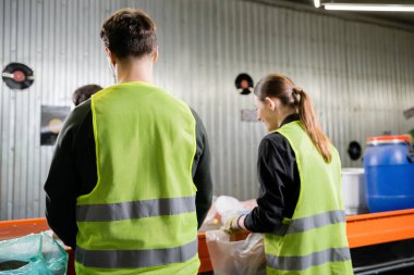 Arka plandaki çöp tasnif merkezi, çöp ayıklama ve geri dönüşüm konsepti yakınlarındaki çöpleri ayıran yüksek görüş mesafesi olan koruyucu yelek giyen işçiler