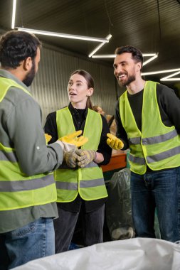 Yüksek görüş yelekleri ve eldivenleri olan pozitif işçiler, çuvala yakın durup atık öğütme istasyonunda birlikte çalışırken Hintli meslektaşlarıyla konuşurken, geri dönüşüm konsepti