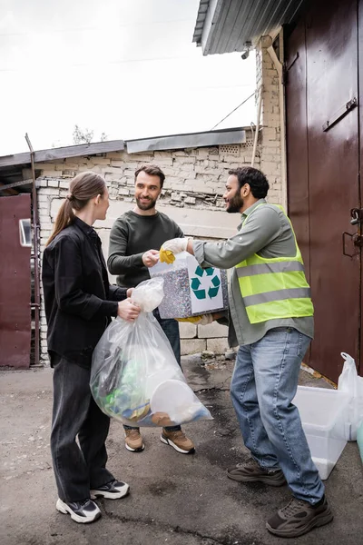 屋外の廃棄物処理場のドアの近くのボランティアからゴミを取って保護ベストでインドの労働者を笑顔 ゴミの分別とリサイクルの概念 — ストック写真