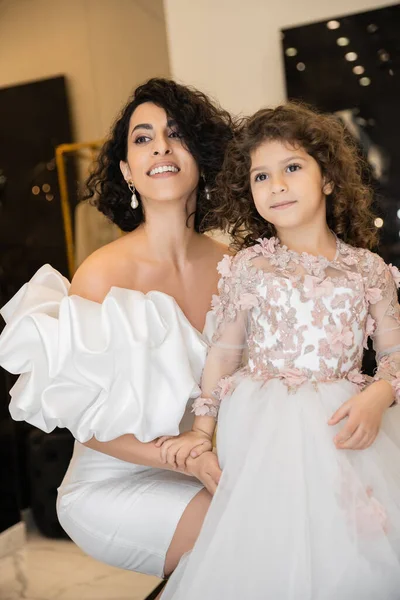 魅惑的な中東の花嫁とともにブルネットの髪で白いウェディングドレスでパフスリーブとフリル抱擁の娘と離れてブライダルストア 特別な機会 — ストック写真