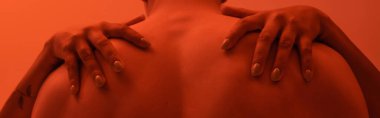 Kıvrımlı, kaslı, kaslı, turuncu arka planda, kırmızı ışık efektiyle onu kucaklayan Afrikalı Amerikalı kadının görüntüsü.
