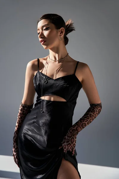 黒エレガントなドレス 動物のプリント手袋 シルバーアクセサリー 世代Zとグレーの背景にポーズトレンディーな春の衣装で若いとエレガントなアジアの女性 — ストック写真