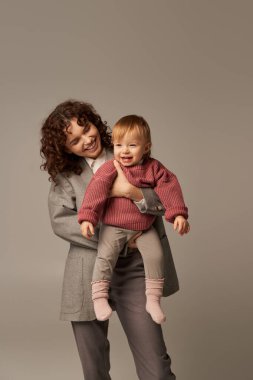 kariyer ve aile, takım elbiseli neşeli anne gri arka planda gülümseyen çocuk, mesleki başarı, sevgi dolu annelik, yaşam tarzı, çoklu görev, kaliteli zaman, iş hayatı dengesi konsepti 
