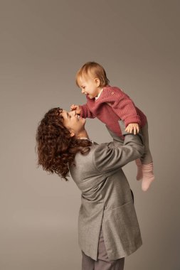 Çalışan anne, ebeveynlik ve kariyer, neşeli iş kadını küçük kızını gri arka planda kaldırıyor, iş hayatı uyum konsepti, sevgi dolu annelik, kaliteli aile zamanı 