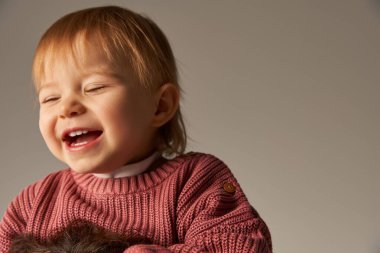 Şirin bir kızın portresi, küçük bir çocuk, günlük giysiler içinde mutlu küçük bir çocuk stüdyoda gri arka planda gülümsüyor, duygu, masumiyet, bebek modası, şık kıyafetler, pembe süveter 
