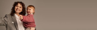 kariyer ve aile, annelik, kaliteli aile zamanı, mutlu ve kıvırcık kadın kollarında küçük kızı gri arka planda, iş ve yaşam arasında denge kuruyor, pozitiflik, afiş 