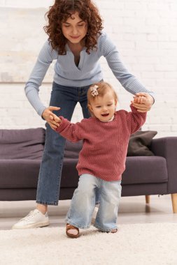 first steps, quality time, bonding, balancing work and life, family relationships, working mother holding hands with toddler daughter, togetherness, cozy living room, denim jeans, casual attire clipart