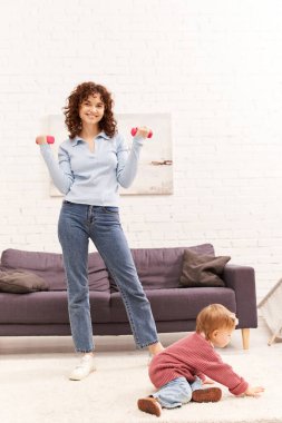 zaman yönetimi, çalışan anne, dengeli yaşam tarzı, kıvırcık kadın halterli kızıyla birlikte rahat oturma odasında, evde çalışma, spor, meşgul anne, fiziksel aktivite 
