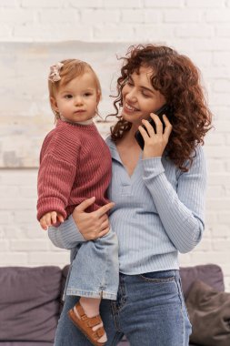 Mutlu genç bir kadın kucağında kucağında küçük kız ve akıllı telefonla konuşuyor, işle hayat arasında denge kuruyor, modern ebeveynlik, ilişkiler, anne kız bağı, uzaktan çalışma, kariyer ve aile arasında denge kuruyor. 