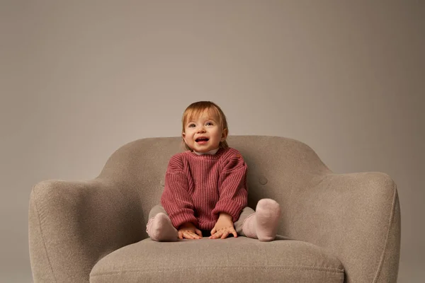 かわいい赤ちゃんの女の子 スタジオ 無邪気さ 小さな子供 幼児のファッション スタイリッシュな衣装 セーターの灰色の背景に快適なアームチェアに座っているカジュアルな服装の幼児 — ストック写真