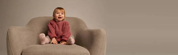かわいい赤ちゃんの女の子 スタジオ 無邪気さ 小さな子供 幼児のファッション スタイリッシュな衣装 バナーの灰色の背景に快適なアームチェアに座っているカジュアルな服装の幼児 — ストック写真