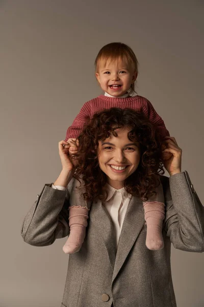 工作生活平衡 快乐的工作母亲 肩上背着孩子 女人和灰色背景的快乐孩子 工作生活和谐的概念 爱的母性 高质量的时间 — 图库照片