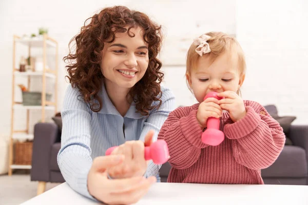 时间管理 工作母亲 平衡的生活方式 卷曲的女人在舒适的客厅里抱着粉红的哑铃 舒适的女儿 家庭锻炼 忙碌的妈妈 现代的养育 — 图库照片