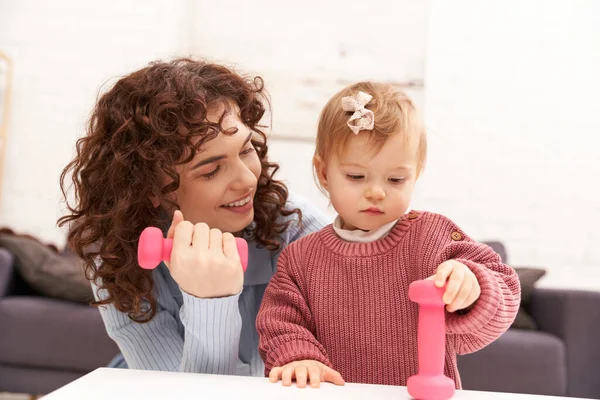 时间管理 有工作的母亲 平衡的生活方式 快乐的女人 在舒适的客厅里带着粉色哑铃与幼儿女儿一起运动 家庭锻炼 忙碌的妈妈 现代的养育 — 图库照片